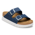 A single double-strap slide sandal shown on a clean white background. The sandal features navy blue suede-like straps with silver-tone metal buckles, a tan cork-textured footbed, and a thick white outsole.
