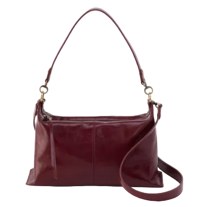 A leather shoulder hobo bag in a maroon color with brushed antique brass hardware and a suede and leather lining.